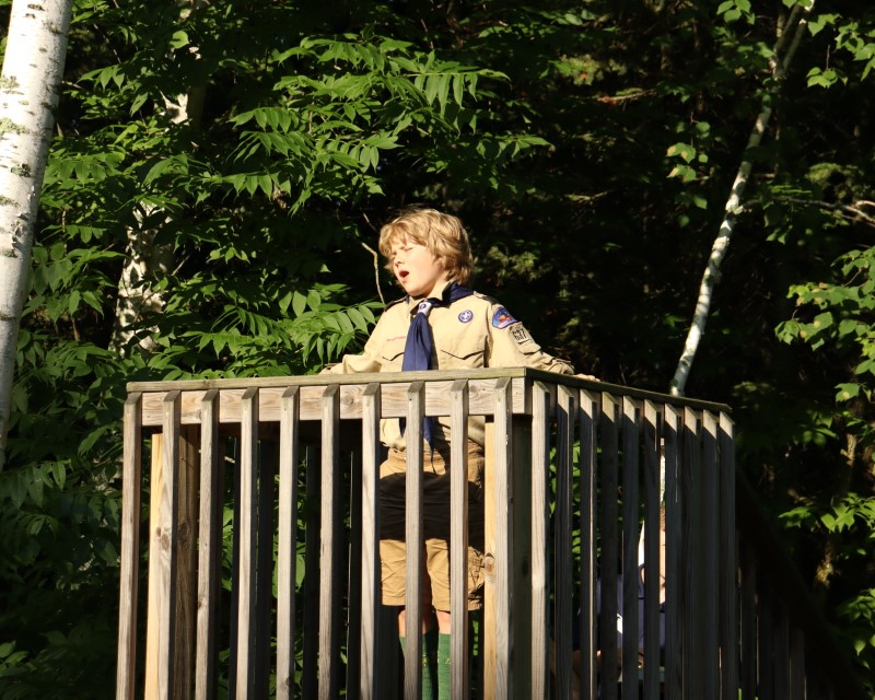 A Scout on an outdoor stage speaking while facing the sun