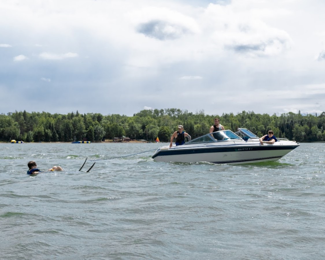 A Scout in the water getting ready to get up on the skis while the boat with the other Scouts and staff member get into position
