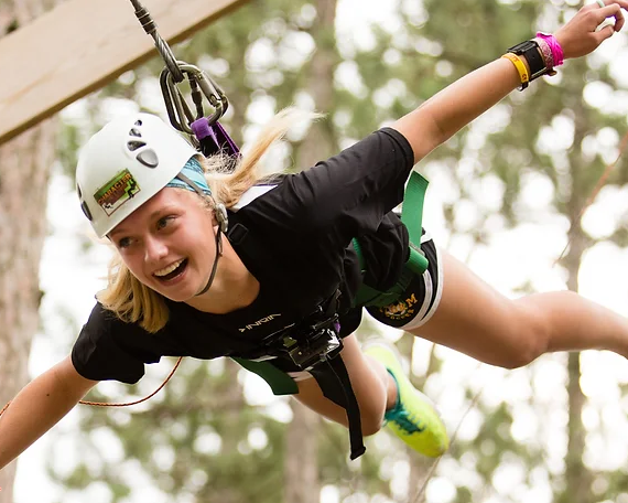 A girl in a helmet and harness is flying through the air, held there by a rope attached to the harness