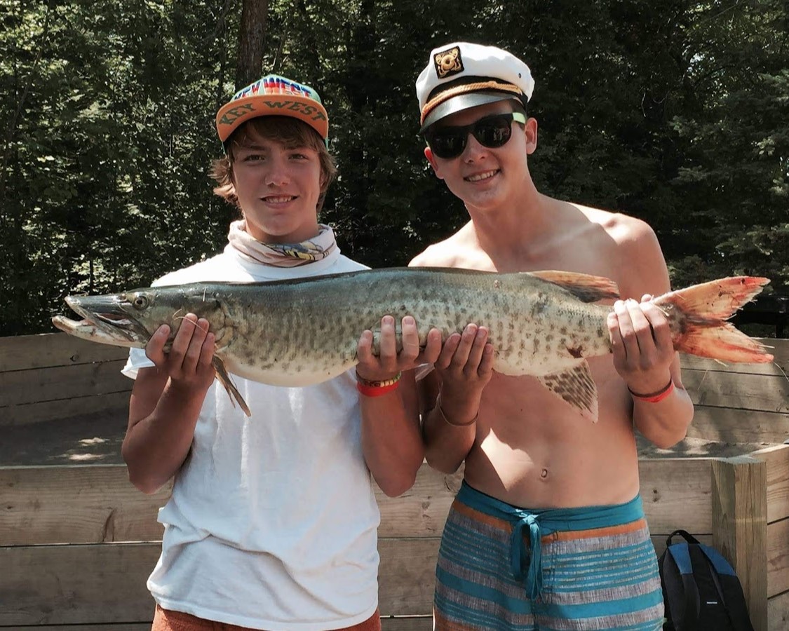 Two Scouts smiling while holding a large (approximately 2 feet long) fish