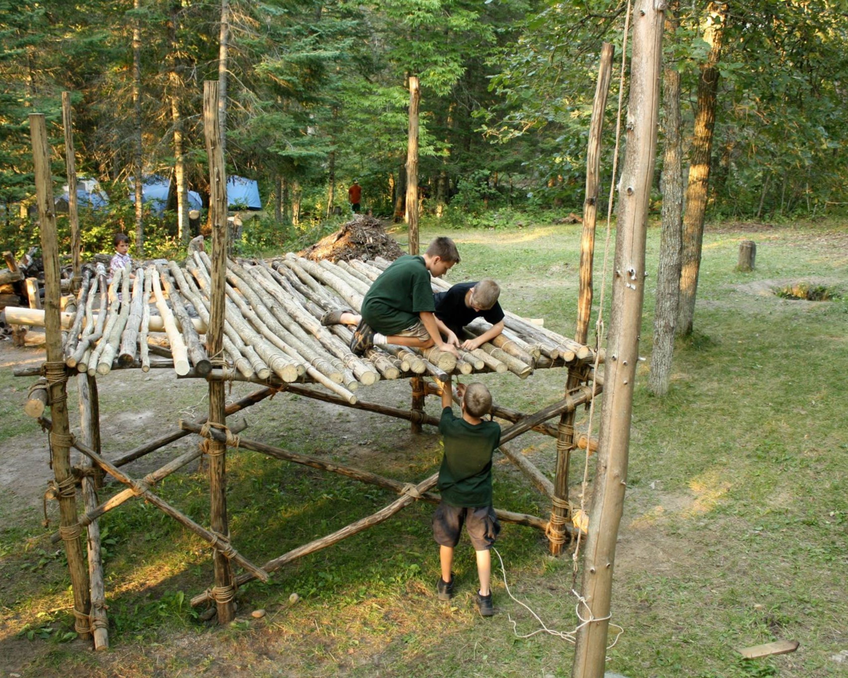 A group of Scouts are lashing together a platform whose top is around 4 feet off of the ground