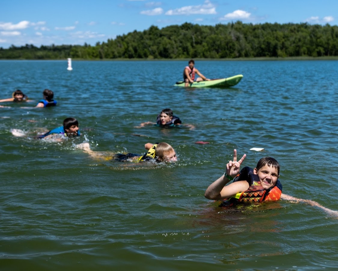 Scouts swimming in a line while a staff member supervises