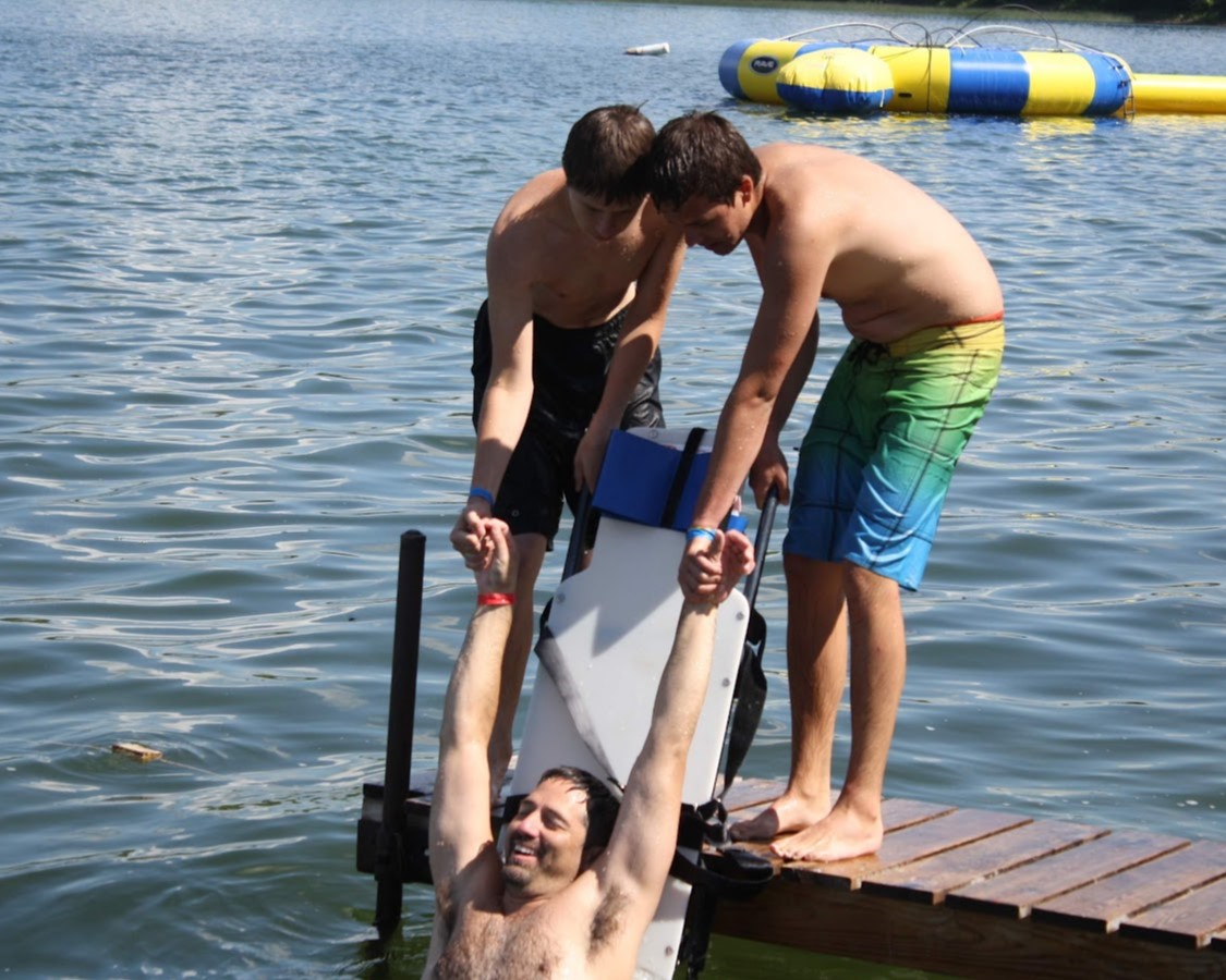 Two Scouts are practicing pulling an adult leader out of the water and onto a backboard without bending their back in case of a spinal injury