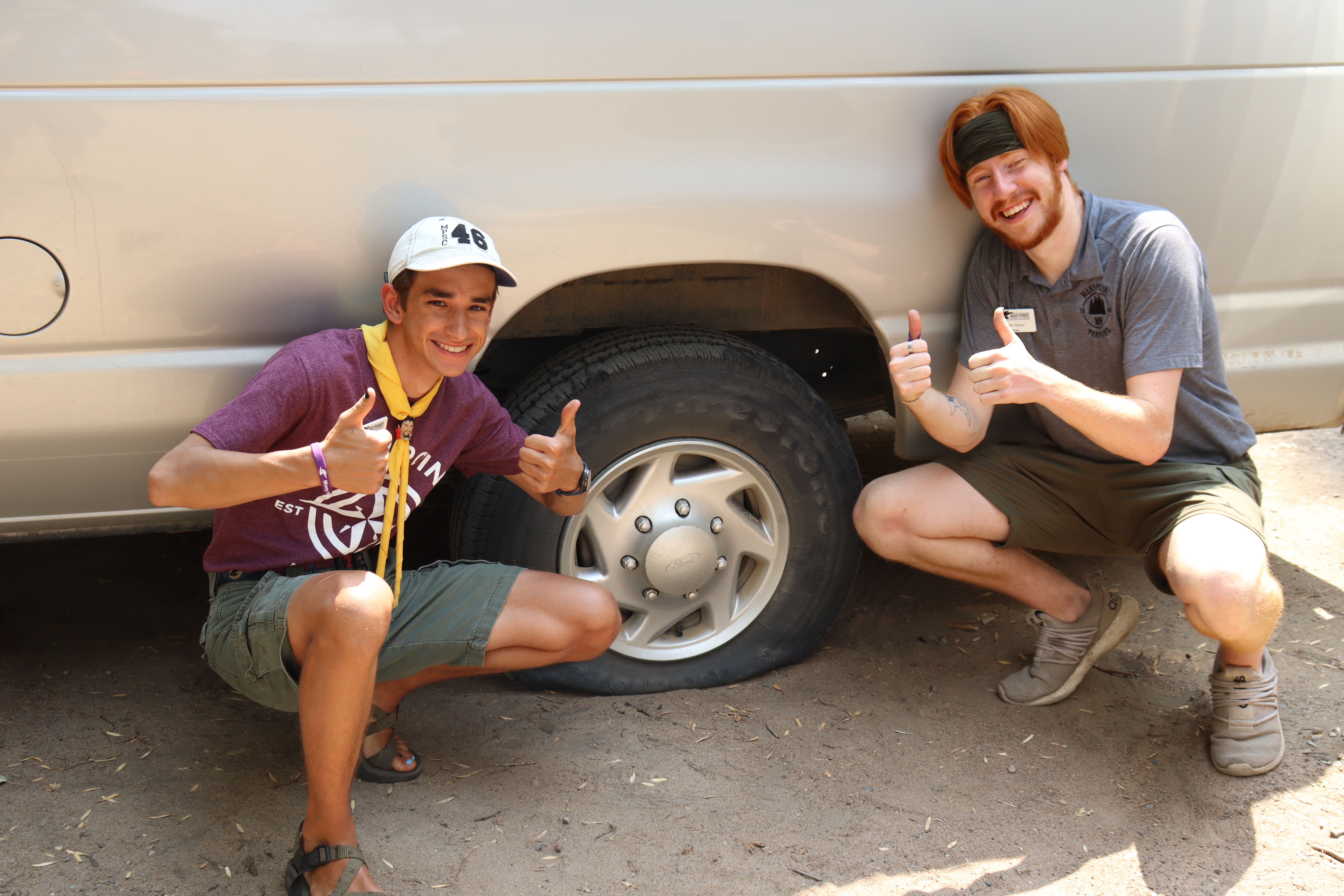 Two staff members posing next to a flat tire